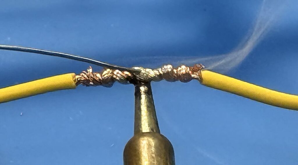 Automotive wire soldering setup with iron, solder, and wires on workbench