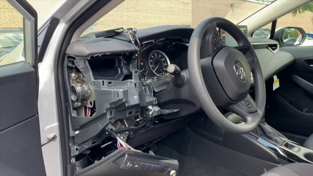 A compact GPS tracker device sits on the dashboard of a modern Toyota Corolla.