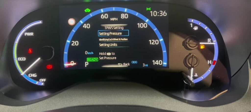 Digital tire pressure gauge on a workbench in a garage with a car behind