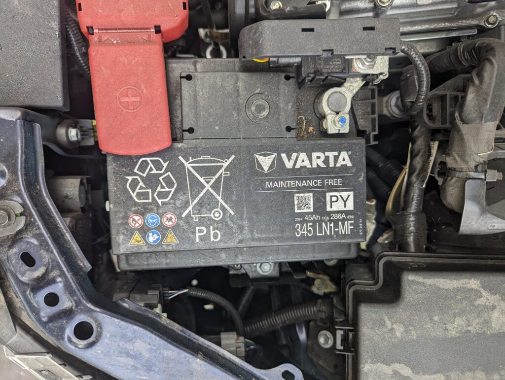 Mechanic installing a new 12V battery replacement in a modern Toyota Corolla engine bay.
