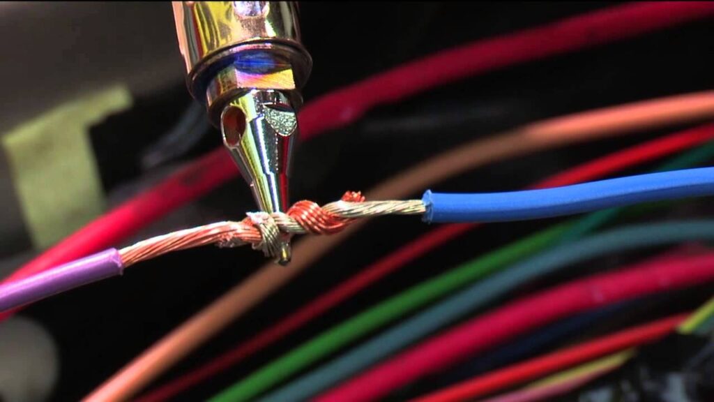 Solder wire spool beside stripped automotive copper wire on a workbench
